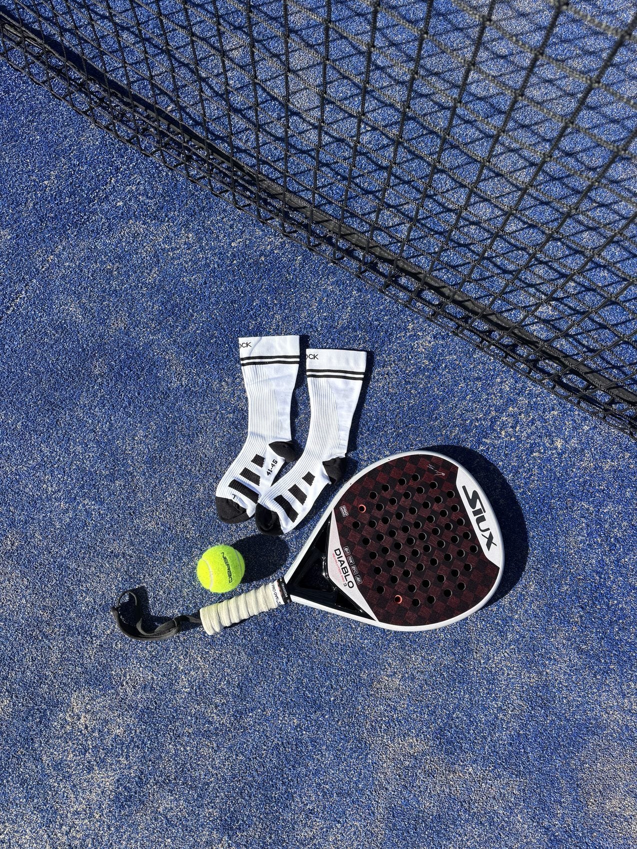 Osock sokken, padelracket en bal op een blauwe padelbaan