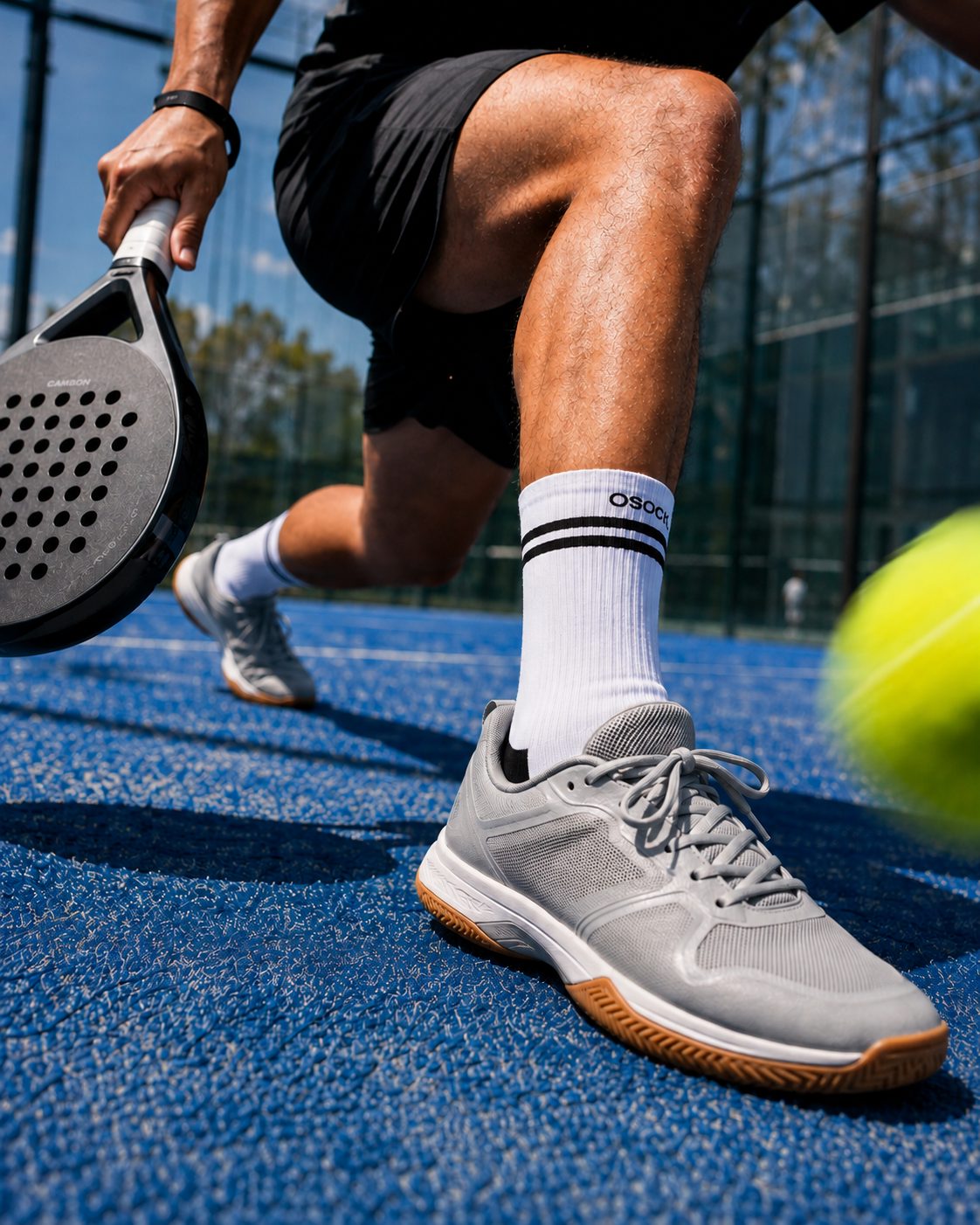 Padelspeler met witte sportsokken op een blauwe baan, vlak voor een lage bal